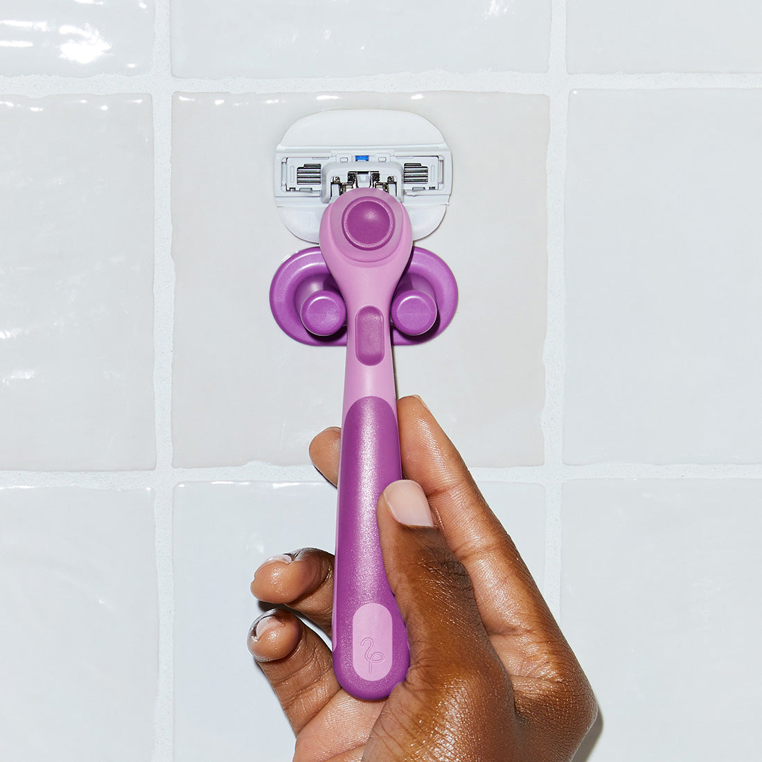 Hand grasping the Fig Moisture Plus razor in its holder on tiled shower wall.